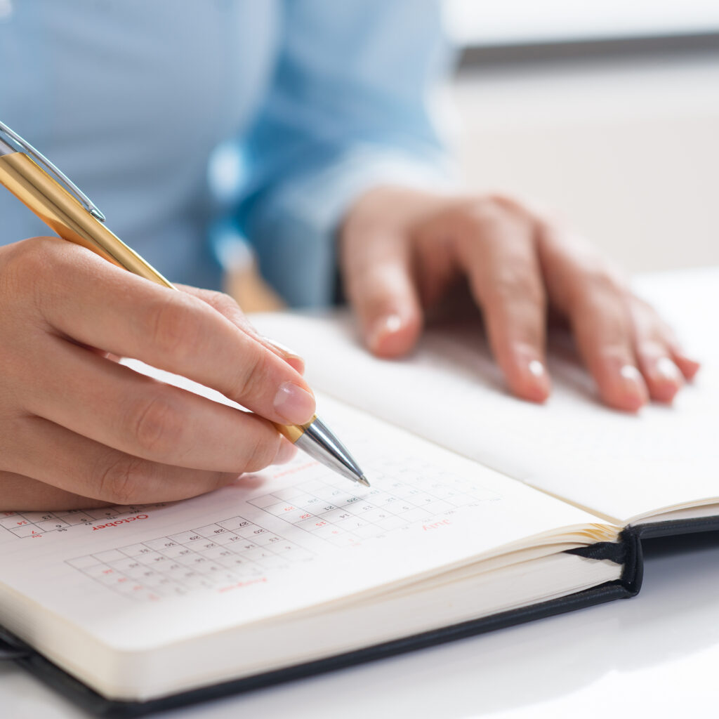 Closeup of woman using diary and scheduling. Entrepreneur sitting at desk. Planning concept. Cropped view.