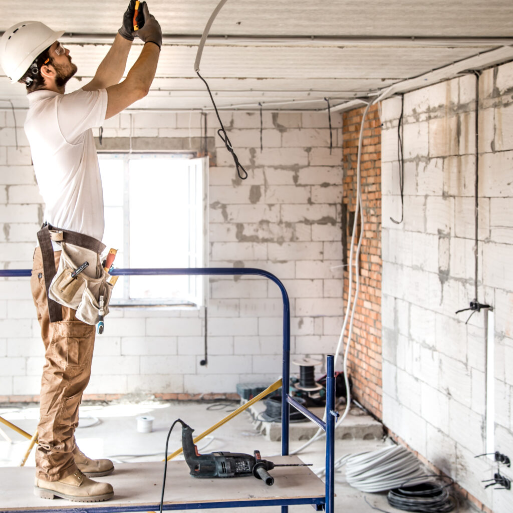 Electrician installer with a tool in his hands, working with cable on the construction site. Repair and handyman concept. House and house reconstruction.