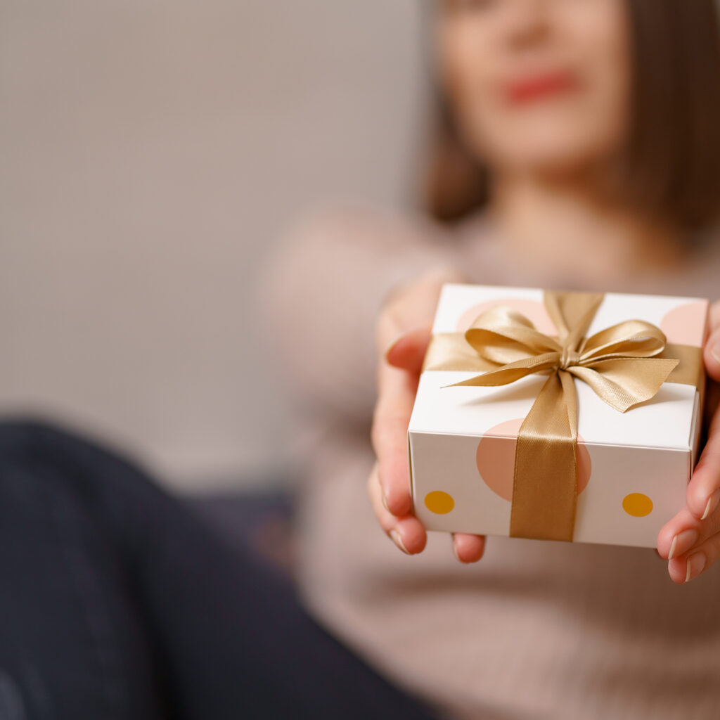 Woman hands holding wrapped white box with golden bow, focus on box