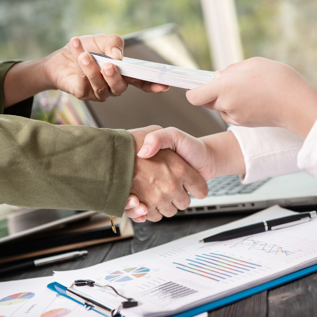 Business people shaking hands, finishing up meeting. businessman giving money to his partner while making contract - bribery and corruption concepts.